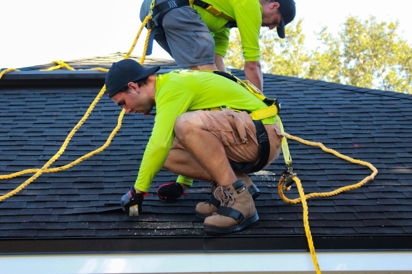 Roofer with a safety harness installing shingles